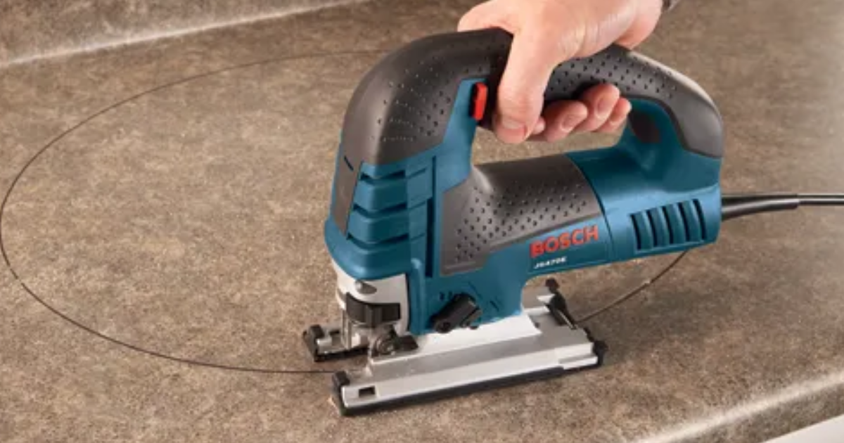 A Bosch JS470E corded jigsaw cutting a curved line in a worktop, with its large footplate flat on the surface and the mains cable running off to the right