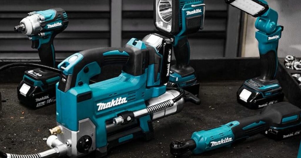 A Makita 18V LXT cordless tool range laid out on a dark workbench: impact wrench, grease gun, two work lights, a cordless ratchet, spare battery packs and sockets