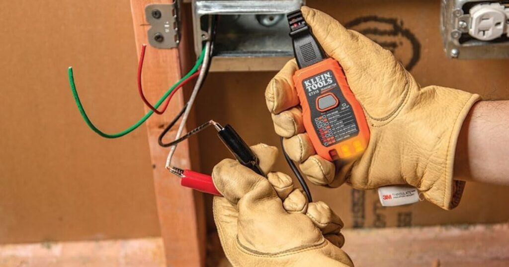 Gloved hands clipping a Klein Tools ET310 circuit tracer transmitter onto conductors in an open junction box