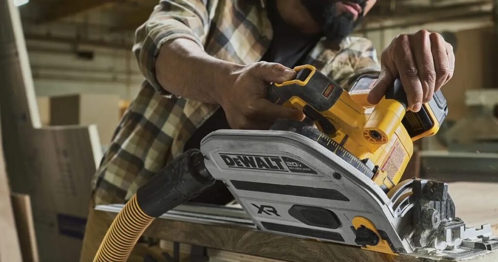 A DeWalt 20V MAX XR cordless plunge track saw running on its guide rail with a dust extraction hose attached, cutting a timber board