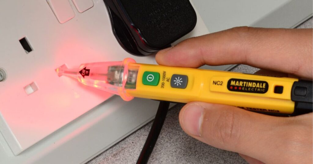 A Martindale NC2 non-contact voltage tester glowing red as it is held against a white mains socket outlet