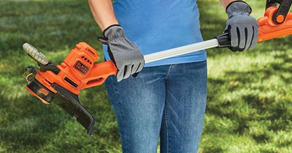 A person in gardening gloves joining the two halves of a BLACK+DECKER cordless string trimmer shaft on a lawn