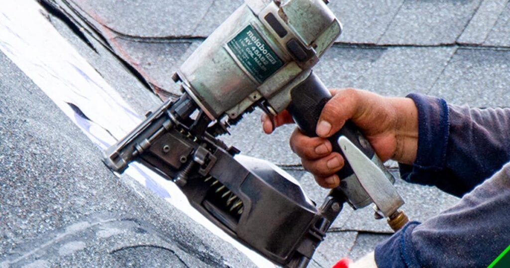 A well-used Metabo HPT NV45AB2 pneumatic coil roofing nailer held against roofing felt and shingles, with the air line fitting visible at the base of the handle