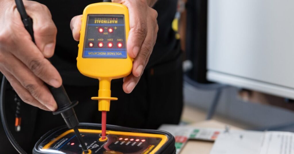 An electrician proving a Martindale two-pole voltage indicator on a proving unit, the voltage LEDs lit across the 50V to 690V scale
