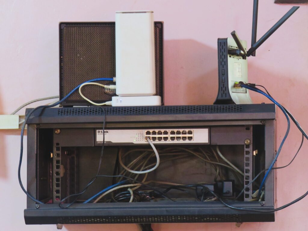 A wall-mounted home network cabinet holding two routers, a network switch and a tangle of ethernet cables
