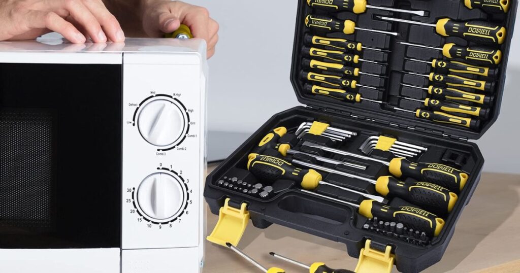 An open hard case of screwdrivers and hex keys beside a white microwave oven being repaired on a kitchen worktop