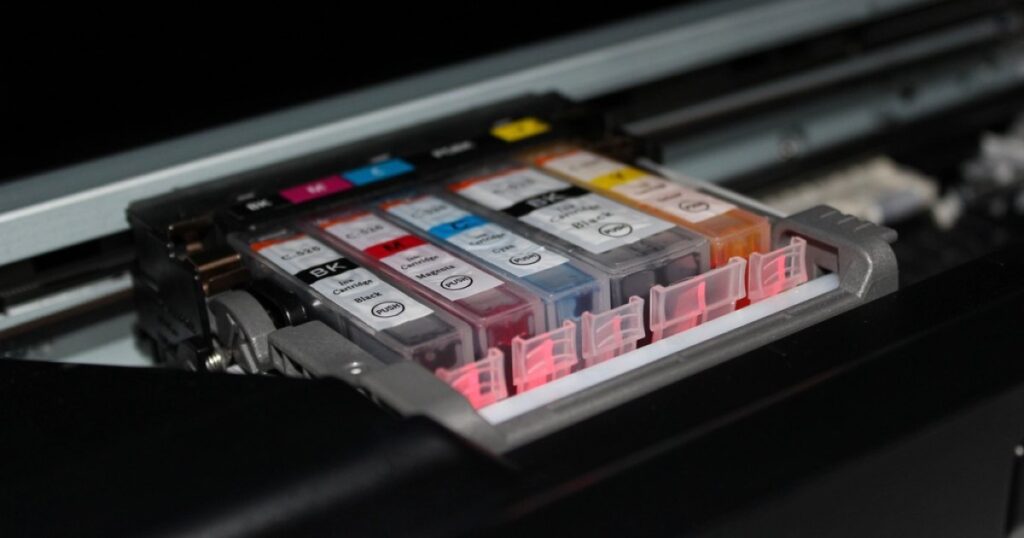 A row of compatible black, cyan, magenta and yellow ink cartridges seated in the print-head carriage of an inkjet printer
