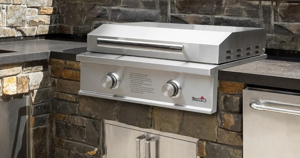 Stanbroil 28-inch built-in natural gas griddle installed in a stone outdoor kitchen island, lid closed, with two control knobs on the stainless front panel